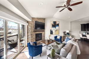 Living room with vaulted ceiling, wood finished floors, ceiling fan, a fireplace, and recessed lighting