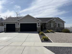 View of front facade featuring stucco siding, fence, stone siding, an attached garage, and driveway