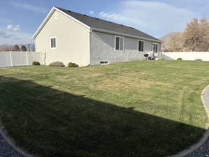 Back of house with a mountain view, a yard, a fenced backyard, and stucco siding