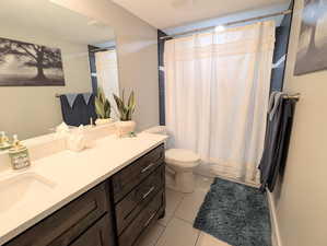 Full bath featuring tile patterned flooring, toilet, vanity, and shower / bath combination with curtain