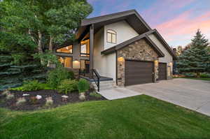 View of front of property with stone siding, stucco siding, concrete driveway, a yard, and an attached garage
