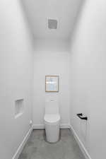 Bathroom with visible vents, baseboards, concrete flooring, and toilet