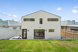 Rear view of property featuring a yard, stucco siding, and fence