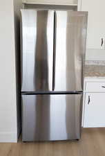 Room details featuring white cabinetry, light wood-type flooring, freestanding refrigerator, and light stone countertops