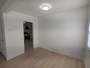 Spare room featuring light wood-style floors, visible vents, and baseboards