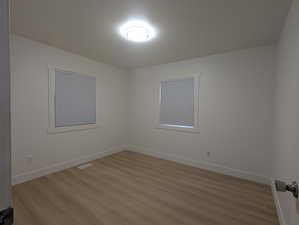 Empty room featuring light wood-style floors, baseboards, and visible vents