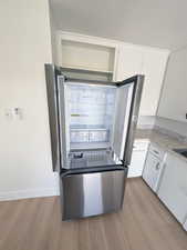 Kitchen featuring smart refrigerator, white cabinets, light wood-style floors, and baseboards