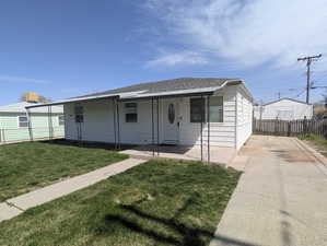 View of front of property featuring a front yard, fence, a shingled roof, and driveway