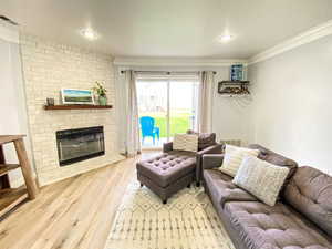 Living area with a brick fireplace, visible vents, crown molding, and wood finished floors
