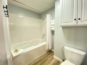 Bathroom with toilet, wood finished floors, baseboards, and a combined bath / shower with jetted tub
