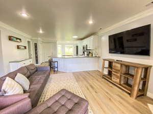 Living room with visible vents, baseboards, light wood-style floors, crown molding, and recessed lighting