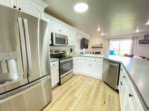 Kitchen featuring white cabinets, a sink, light wood-type flooring, a peninsula, and stainless steel appliances