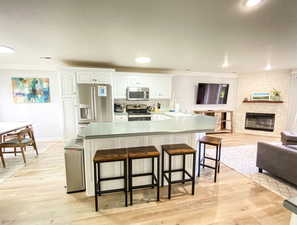 Kitchen featuring white cabinetry, stainless steel appliances, open floor plan, light wood finished floors, and a breakfast bar area