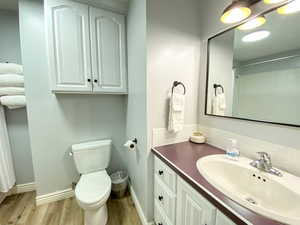 Full bathroom featuring toilet, wood finished floors, vanity, and baseboards