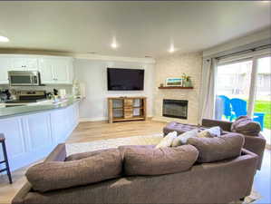 Living area featuring baseboards, a brick fireplace, ornamental molding, light wood-type flooring, and recessed lighting