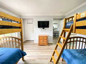 Bedroom with light wood finished floors, baseboards, and ornamental molding