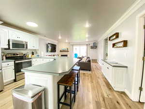 Kitchen with a breakfast bar, white cabinetry, ornamental molding, and appliances with stainless steel finishes