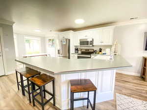 Kitchen with a kitchen bar, light wood-type flooring, appliances with stainless steel finishes, and visible vents