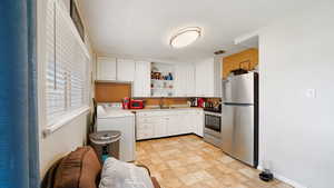 Kitchen with washer / clothes dryer, open shelves, white cabinets, stainless steel appliances, and a sink