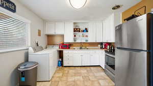 Kitchen featuring open shelves, white cabinets, a sink, stainless steel appliances, and washer and clothes dryer
