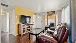 Living area with dark wood-type flooring, baseboards, and visible vents