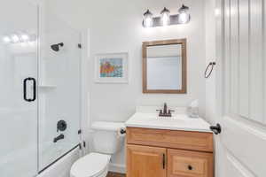 Bathroom with combined bath / shower with glass door, toilet, and vanity