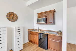 Kitchen with wine cooler, stainless steel microwave, light wood-style floors, and a sink