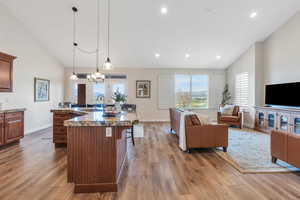 Kitchen with wood finished floors, a sink, open floor plan, a breakfast bar area, and a spacious island