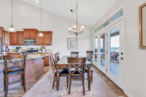 Dining room with light wood-style flooring, high vaulted ceiling, an inviting chandelier, and baseboards