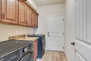 Clothes washing area featuring cabinet space, baseboards, light wood finished floors, and washing machine and dryer