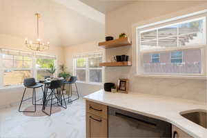 Kitchen featuring marble finish floor, stainless steel dishwasher, light stone countertops, pendant lighting, and a chandelier