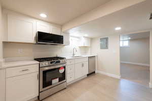 Kitchen with stainless steel appliances, light countertops, a sink, and white cabinetry