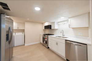 Kitchen featuring white cabinets, stainless steel appliances, visible vents, a sink, and washing machine and dryer
