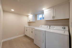 Clothes washing area with light wood-type flooring, baseboards, visible vents, cabinet space, and washer and dryer