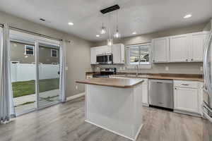 Kitchen with white cabinets, a center island, a sink, appliances with stainless steel finishes, and light wood-style floors