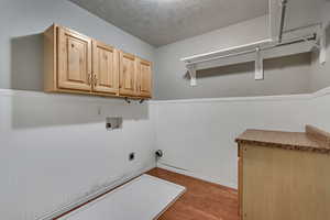 Laundry area with washer hookup, hookup for an electric dryer, wood finished floors, cabinet space, and a wainscoted wall