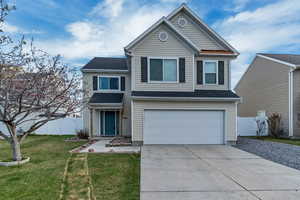 Traditional-style home with an attached garage, fence, a front lawn, driveway, and roof with shingles