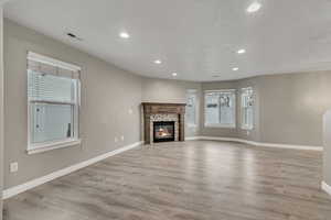 Unfurnished living room featuring visible vents, baseboards, a tiled fireplace, recessed lighting, and light wood-style flooring