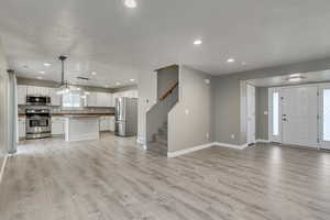 Interior space featuring a sink, open floor plan, appliances with stainless steel finishes, white cabinetry, and light wood-style flooring