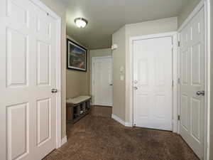 Hallway with baseboards, dark colored carpet, and a textured ceiling