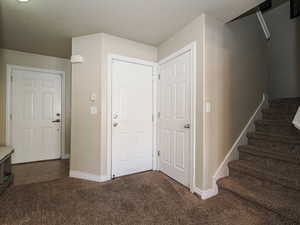 Carpeted entryway featuring tile patterned floors, stairway, visible vents, and baseboards