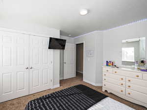 Carpeted bedroom with a closet, a textured ceiling, and baseboards