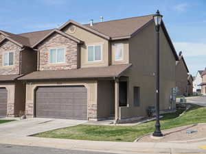 View of front of property featuring an attached garage, concrete driveway, stucco siding, and stone siding