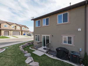 Rear view of property with a lawn, central AC, and stucco siding