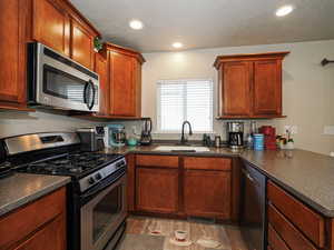 Kitchen featuring a peninsula, a textured ceiling, dark countertops, appliances with stainless steel finishes, and a sink