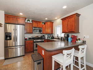 Kitchen featuring a sink, dark countertops, appliances with stainless steel finishes, a kitchen bar, and a peninsula