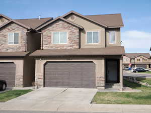 View of property featuring stone siding, a garage, stucco siding, driveway, and roof with shingles