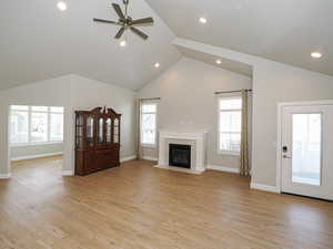 Unfurnished living room featuring light wood-type flooring, ceiling fan, a fireplace, and lofted ceiling