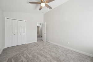 Unfurnished bedroom with a closet, baseboards, ceiling fan, carpet, and vaulted ceiling