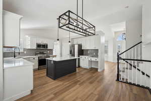 Kitchen with white cabinets, a sink, light countertops, appliances with stainless steel finishes, and wood finished floors